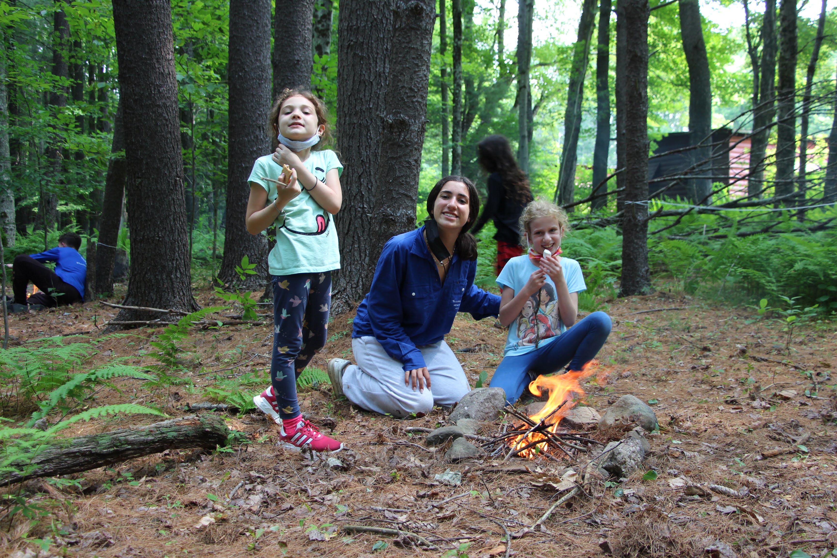 counselor and 2 campers roasting marshmallow on a campfire