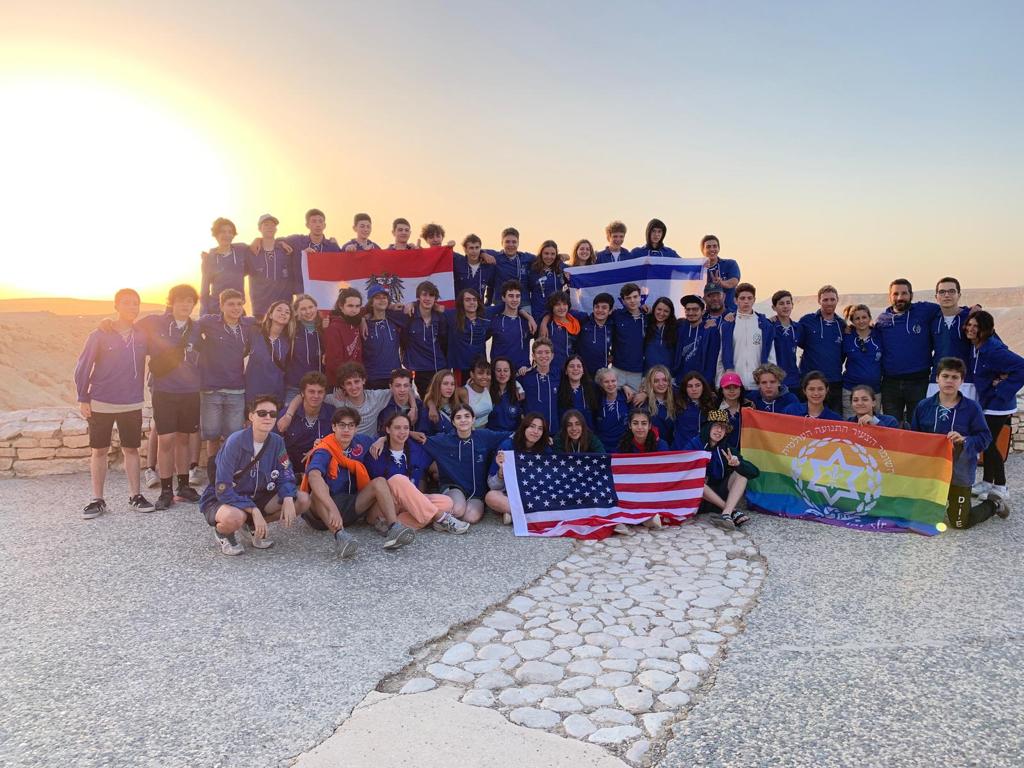 group of participants at masada during sunrise, holding flags from different countries, as well as our program's Pride flag