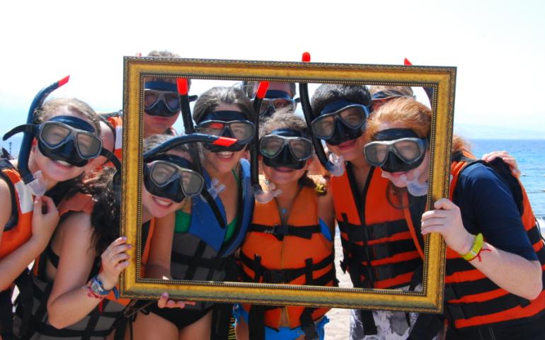Teens with snorkel gear on posing behind an empty picture frame in front of the Mediterranean Sea