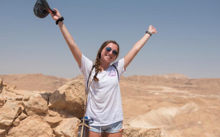 Teen posing with their hands up in excitement. Israel desert is behind them.