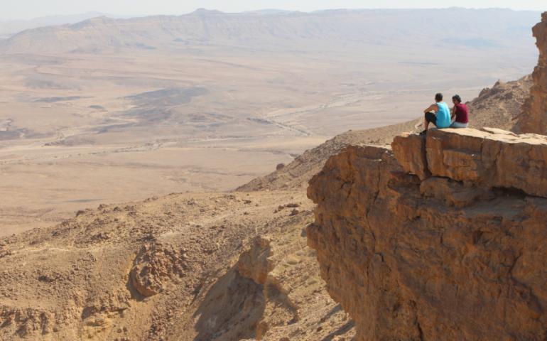 Teens sitting on the side of a cliff overlooking the desert