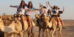 Teens riding camels through the desert