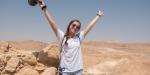Teen posing with their hands up in excitement. Israel desert is behind them.